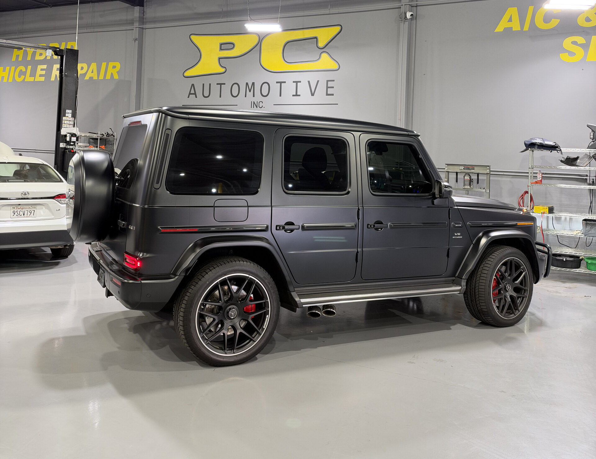 PC Automotive service bay in Rancho Cordova, with the shop's yellow logo on the wall behind a vehicle on the polished floor